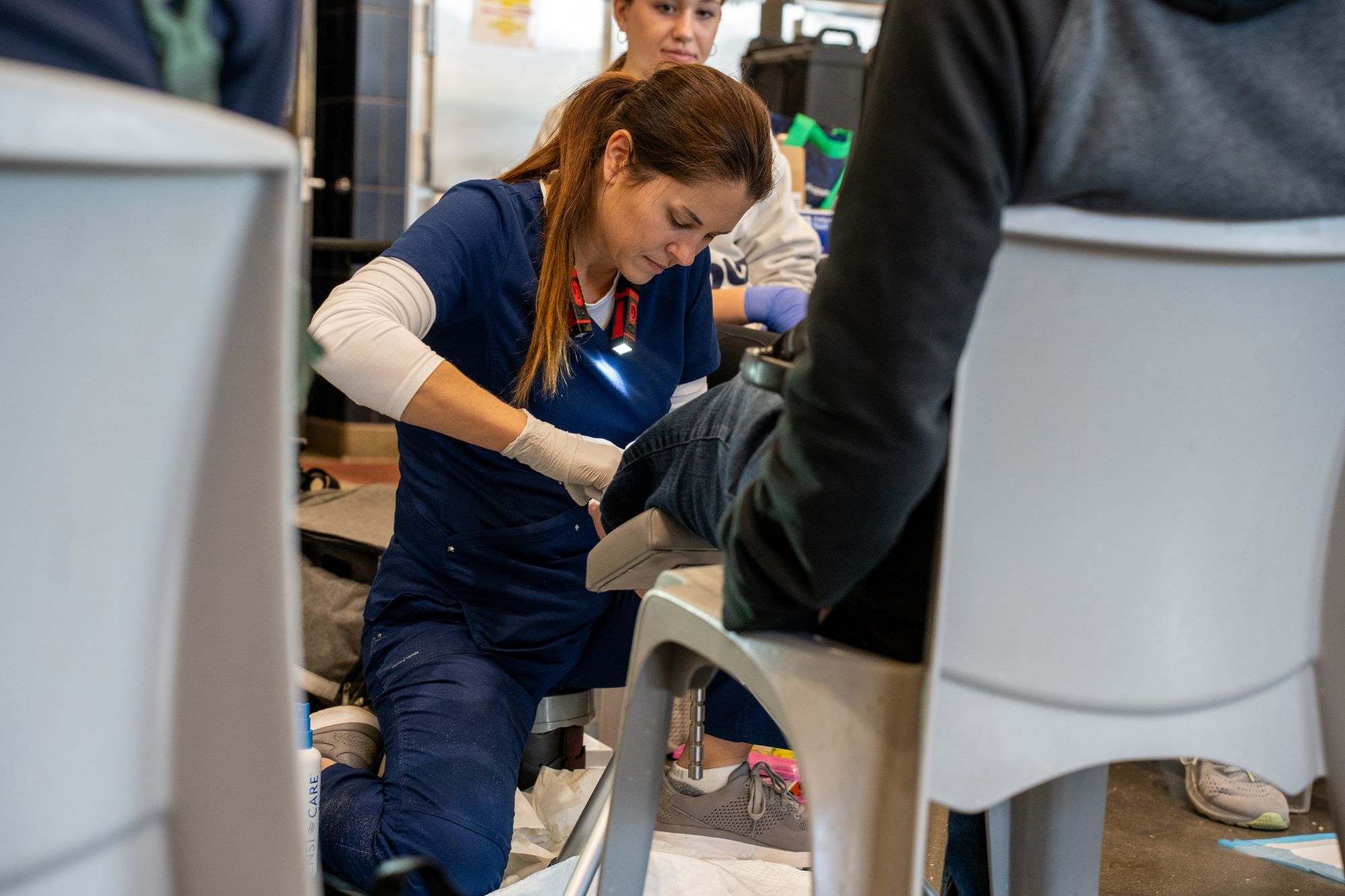 A woman in blue nursing scrubs tends to a person's foot