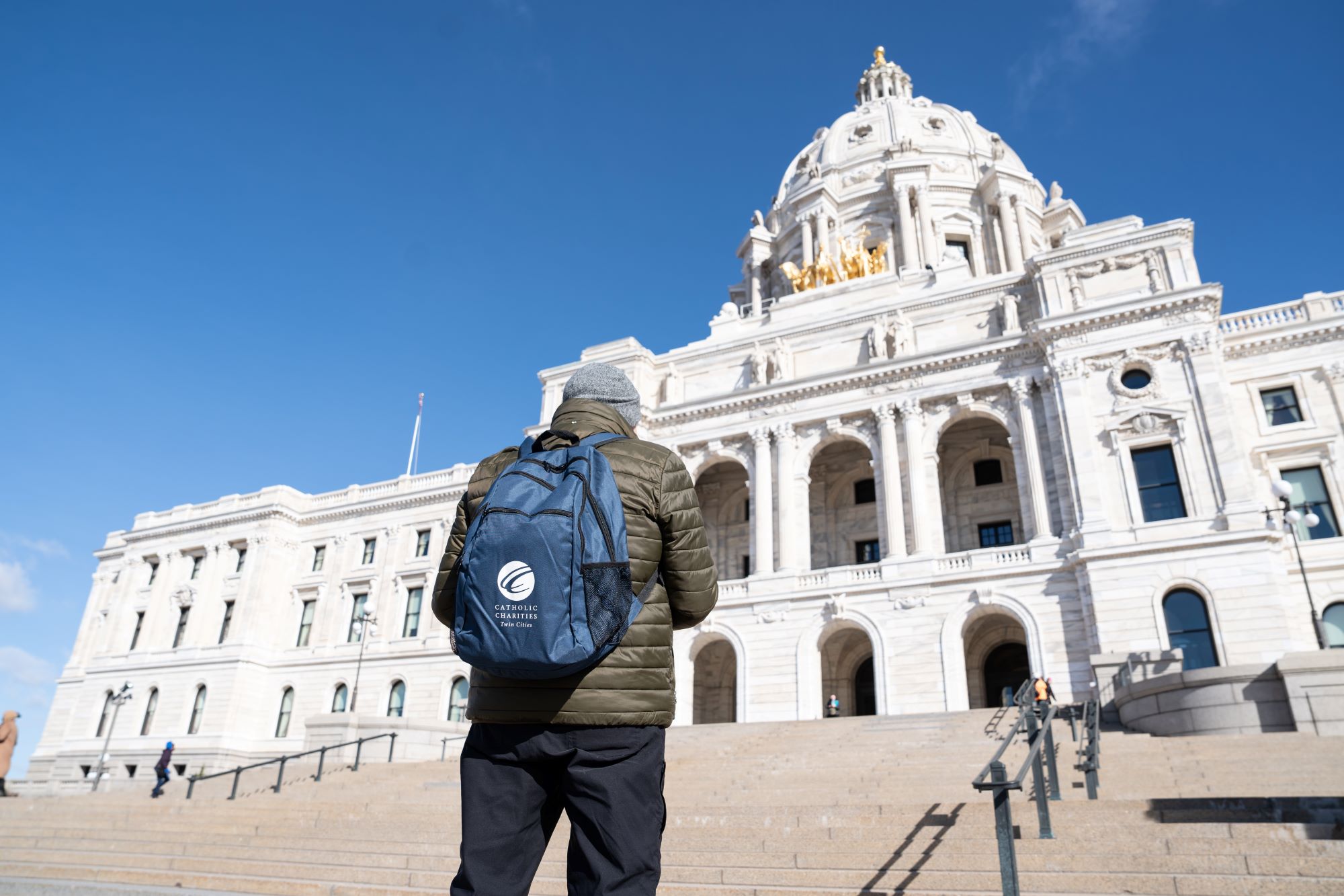 A person with a Catholic Charities backpack stands in front of the Capitol