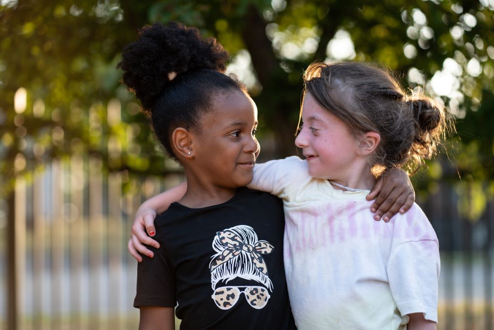 Two little girls smile with their arms around each other.