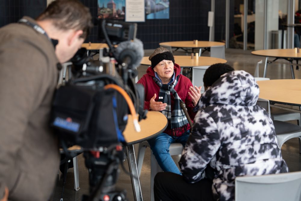 Older woman experiencing homelessness speaks to a reporter and cameraman