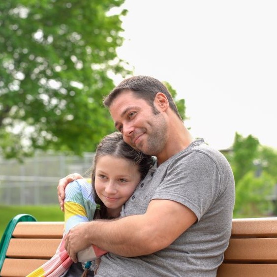 Man hugs girl on a park bench as they both are smiling